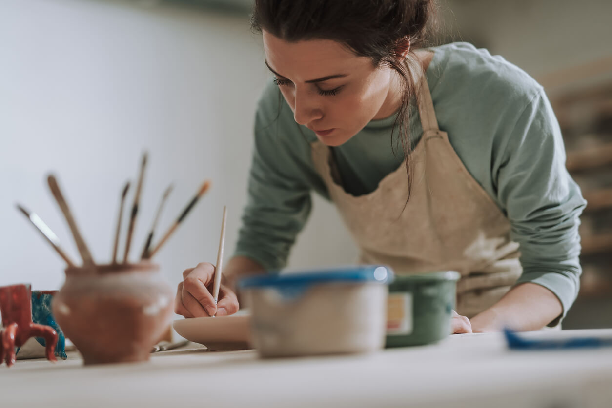 Woman making art, with cup full of paintbrushes.