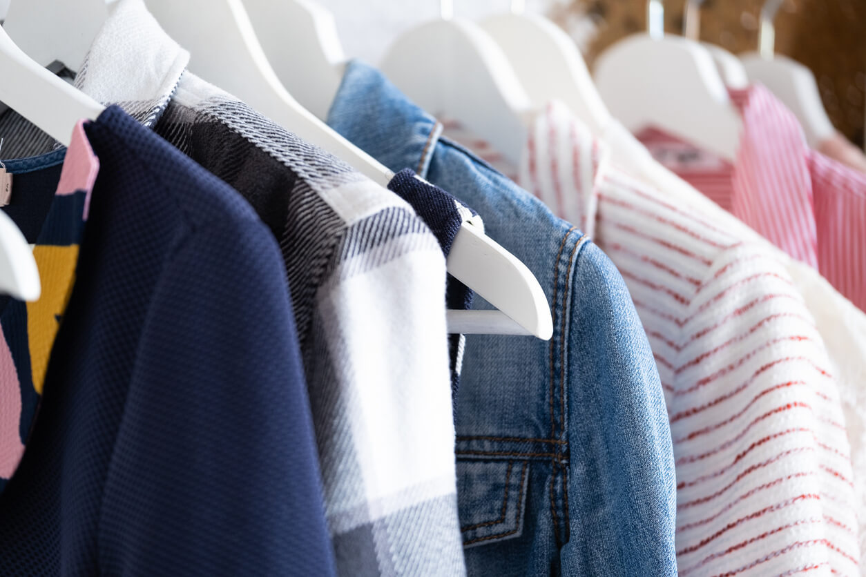 Wooden white hangers with clothes on the rail in the store with women's clothing